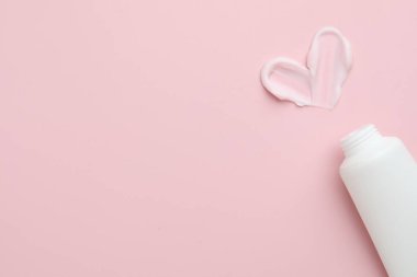 Pembe arka planda nemlendirici krem ve tüpten yapılmış kalp şekli, üst manzara. Metin için boşluk