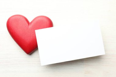Beyaz ahşap masada boş bir kart ve dekoratif bir kalp. Tasarım için model