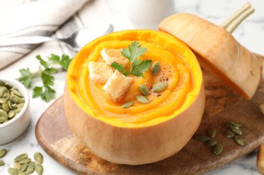 Çekirdekli balkabağı kremalı çorba, maydanoz ve kızarmış ekmekler beyaz masada servis ediliyor, yakın plan.