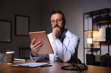 Doktor, gece vardiyası sırasında klinikte tablet üzerinde çalışıyor.