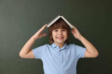 Okula dönelim. Kapalı alanda tahtaya karşı kitap yazan bir çocuk.