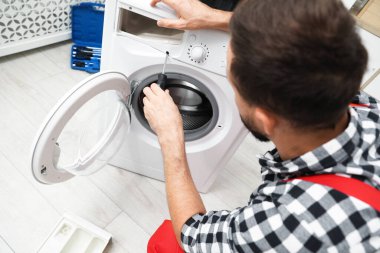 Profesyonel tamirci içeride bozuk çamaşır makinesini tamir ediyor, yakın plan.