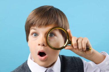 Açık mavi arka planda büyüteç olan küçük çocuk şaşırdı.