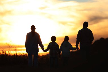Aile gün batımında, arka planda el ele tutuşuyor.