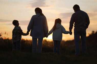 Aile gün batımında, arka planda el ele tutuşuyor.