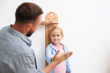 Babası küçük kızının boyunu ölçüyor. Beyaz duvarın yanında. Metin için boşluk