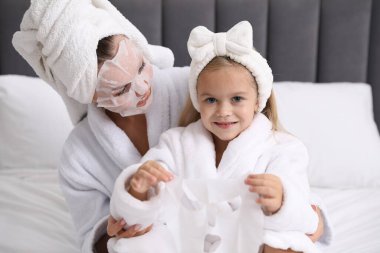 Anne ve kız bornozla evde yüz maskesi takıyor.