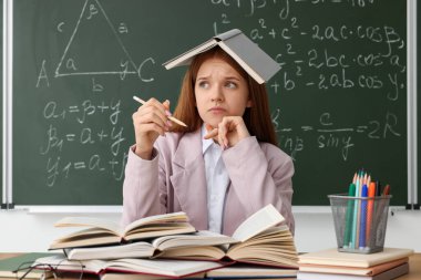 Okula dönelim. Masasında kitap ve kırtasiye malzemesi olan öğrenci içeride matematik ödevi olan yazı tahtasına karşı.