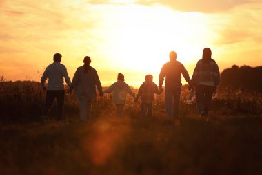 Aile gün batımında, arka planda el ele tutuşuyor.