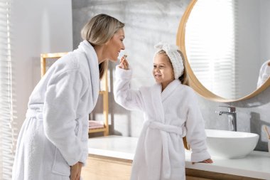 Anne ve kızı banyoda dişlerini fırçalıyorlar.