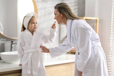 Anne ve kızı banyoda dişlerini fırçalıyorlar.