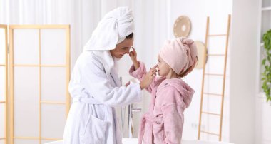 Anne ve kızı banyoda birbirlerine krem sürüyorlar.