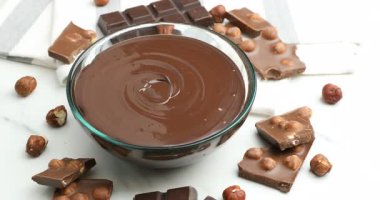 Erimiş çikolata ve beyaz masada fındıklı parçalar dönüyor.