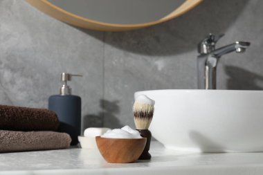 Banyo lavabosunun yanındaki beyaz tezgahta tıraş fırçası ve köpük. Berber aletleri.