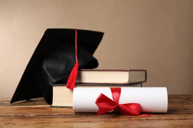 Mezuniyet şapkası, diploma ve kitaplar ahşap masada, yakın plan.