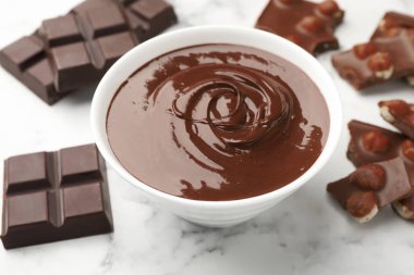 Erimiş çikolata ve parçalarla dolu bir kase beyaz mermer masa, yakın plan.