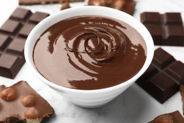 Erimiş çikolata ve parçalarla dolu bir kase beyaz mermer masa, yakın plan.