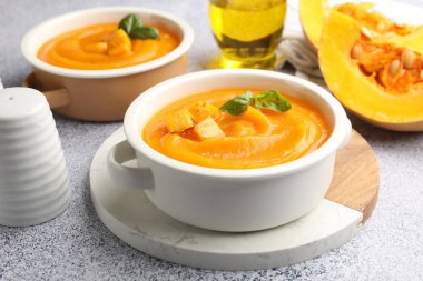 Gri masada servis edilen fesleğenli balkabağı kremalı çorba, yakın plan.