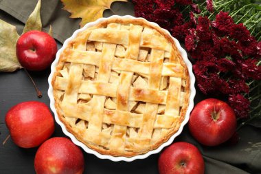 Lezzetli ev yapımı turta, taze elmalar, akçaağaç yaprakları ve siyah ahşap masa üzerinde çiçekler, düz uzanmış