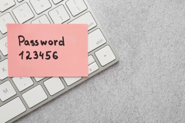 Gri tablonun üstünde parola ve bilgisayar klavyesi olan kağıt not, üst görünüm. Metin için boşluk