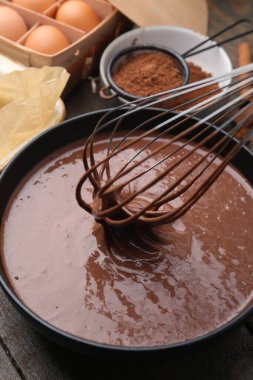 Sıvı çikolata hamurunu ahşap masada çırpma kabıyla karıştırmak, yakın plan.