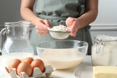 Hamur yapmak (sıvı hamur). Beyaz masada un yiyen bir kadın. Kapalı alanda, yakın plan.