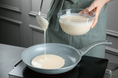 Mutfaktaki gri masada kaseden tavaya sıvı hamur döken kadın, yakın plan.