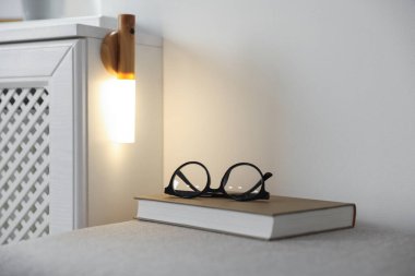 Puf gözlüklü ve evdeki duvarda taşınabilir LED lambalı bir kitap. Metin için boşluk