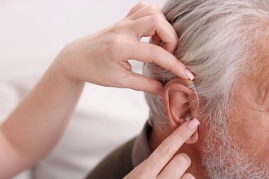 Bakıcı, kıdemli adamın evde işitme cihazı takmasına yardım ediyor.