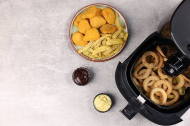 Lezzetli kalamar halkalı kızartma, tavuk nugget, patates kızartması ve soslar gri masada, düz yerde. Metin için boşluk