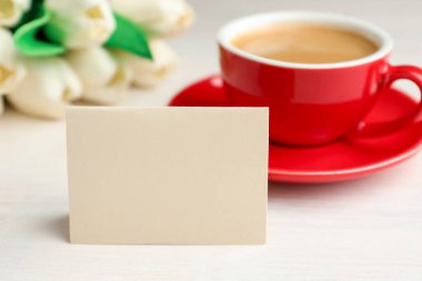 Boş kart, çiçekler ve beyaz ahşap masada bir fincan kahve, yakın plan. Tasarım için model