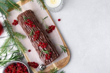 Lezzetli Noel kütüğü (geleneksel Noel pastası) kırmızı üzümlü ve köknar ağacının dalları ışık masasında, düz yatar. Metin için boşluk