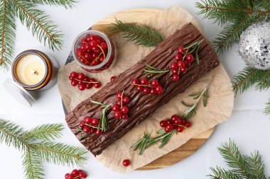 Lezzetli Noel kütüğü (geleneksel Noel pastası) kırmızı frenk üzümü, mum ve köknar ağacı dallarıyla beyaz fayanslı masa, düz yatıyordu