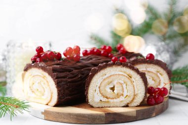 Lezzetli Noel kütüğü (geleneksel Noel pastası) kırmızı üzümlü ve köknar ağacı dallı beyaz masa, yakın plan