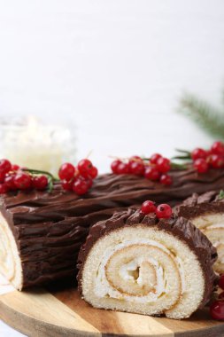 Lezzetli Noel kütüğü (geleneksel Noel pastası) beyaz masa üzerinde kırmızı frenk üzümü, yakın plan. Metin için boşluk