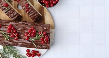 Lezzetli Noel kütüğü (geleneksel Noel pastası) kırmızı frenk üzümü ve köknar dallarıyla beyaz fayanslı masa, düz yatak. Metin için boşluk