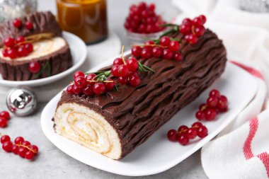 Lezzetli Noel kütüğü (geleneksel Noel pastası) gri masa üzerinde kırmızı frenk üzümü, yakın plan