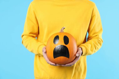 Cadılar Bayramı kutlaması. Açık mavi arka planda çizilmiş ürkütücü yüzlü balkabağı tutan adam, yakın plan.