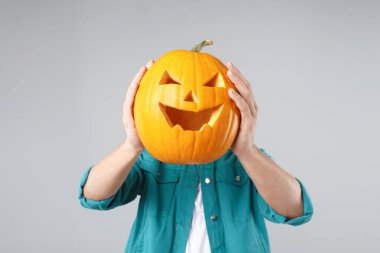 Cadılar Bayramı kutlaması. Açık gri arka planda oyulmuş ürkütücü yüzü olan bir adam balkabağı tutuyor.