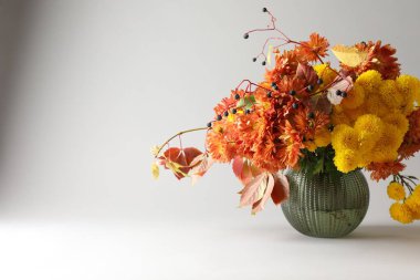 Sonbahar atmosferi. Güzel çiçekli vazo ve açık gri arka planda böğürtlen, yakın plan. Metin için boşluk