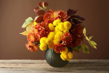 Sonbahar atmosferi. Üzerinde güzel çiçekler ve yapraklar olan bir vazo. Kahverengi arka planda.
