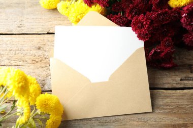 Blank card, envelope and flowers on wooden table, top view. Mockup for design