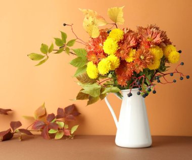 Sonbahar atmosferi. Üzerinde güzel çiçekler, böğürtlen ve yapraklar olan vazo, turuncu arka planda.