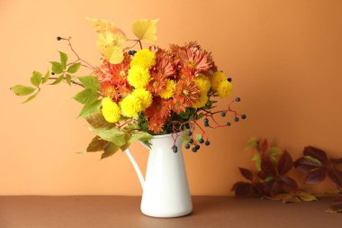 Sonbahar atmosferi. Üzerinde güzel çiçekler, böğürtlen ve yapraklar olan vazo, turuncu arka planda.