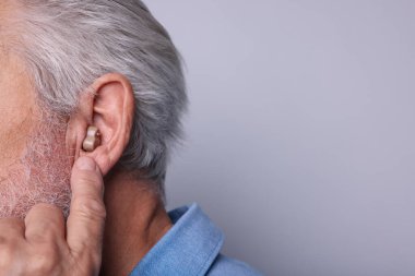 Açık gri arka planda işitme cihazı olan son sınıf öğrencisi, yakın plan.