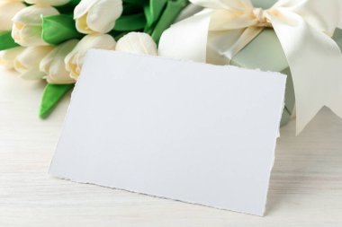 Boş kart, hediye ve çiçekler beyaz ahşap masada, yakın plan. Tasarım için model