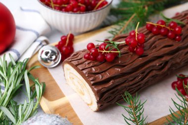 Lezzetli Noel kütüğü (geleneksel Noel pastası) kırmızı frenk üzümü ve köknar ağacı dalları ışık masasında, yakın plan