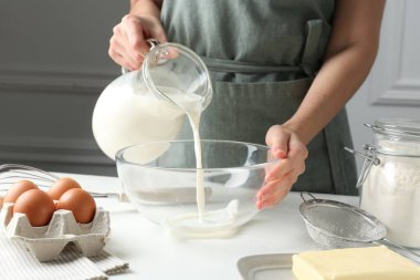 Hamur yapmak (sıvı hamur). Beyaz masadaki kaseye süt döken kadın, yakın plan.