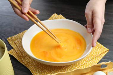 Koyu ahşap masada yumurta çırpan kadın, yakın plan.