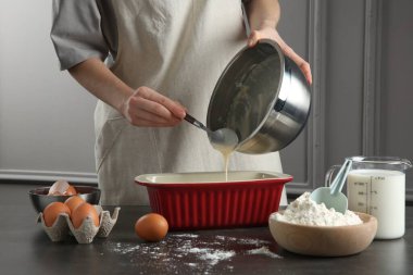 Mutfaktaki gri masada kaseden yemek kabına sıvı hamur döken kadın, yakın plan.